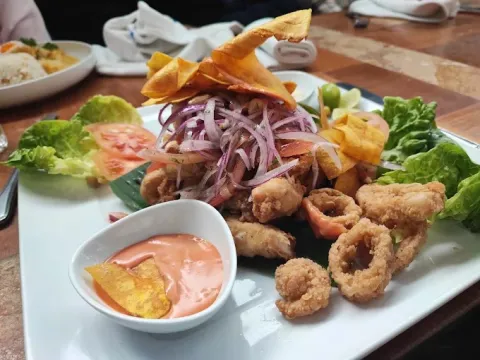 Plato de mariscos fritos acompañado de cebolla morada, lechuga, chips de plátano y salsa cremosa.