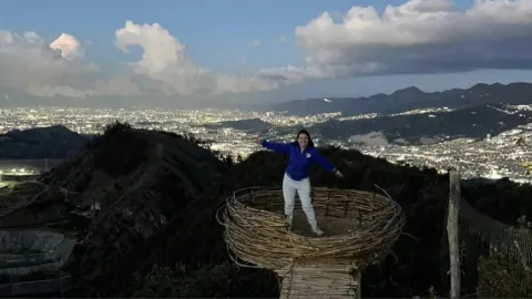 Una visitante disfruta de una experiencia única en un mirador ecológico de montaña, rodeada de imponentes paisajes naturales y una espectacular vista panorámica de Bogotá, donde las montañas se funden con la inmensidad de la ciudad.