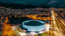 Nighttime panoramic view from above of the Movistar Arena and El Campín Stadium, with the city lights in the background.