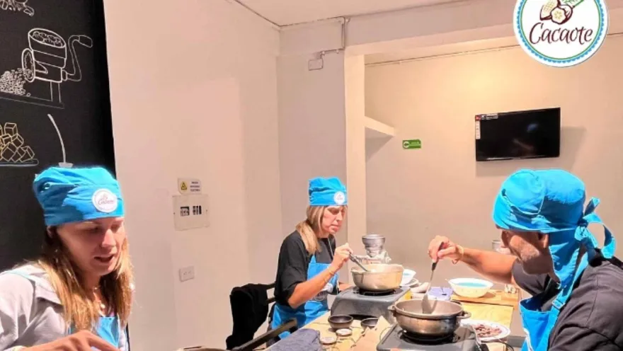 Dos mujeres y un hombre con delantales y gorros azules calientan cacao en sendas ollas.