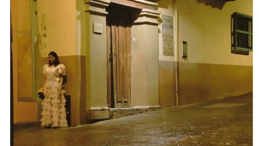  Mujer con cara de demonio y vestida con ropa antigua, detrás de una pared en una calle desolada.