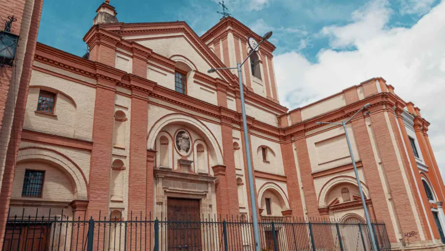 Iglesia San Ignacio fachada completa de lado con un poste eléctrico al frente y el cielo azul con algunas nubes.