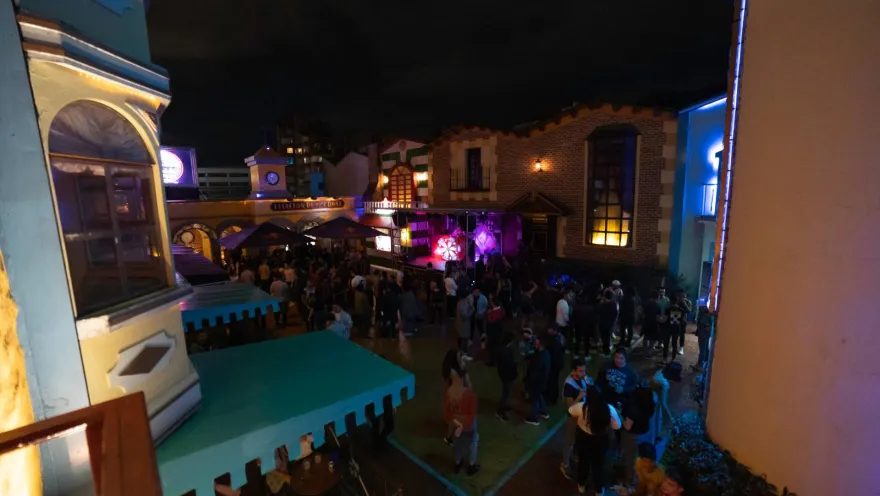 Theatron de noche en plazoleta interior con fachadas de castillos iluminadas y personas que bailan y conversan alrededor.