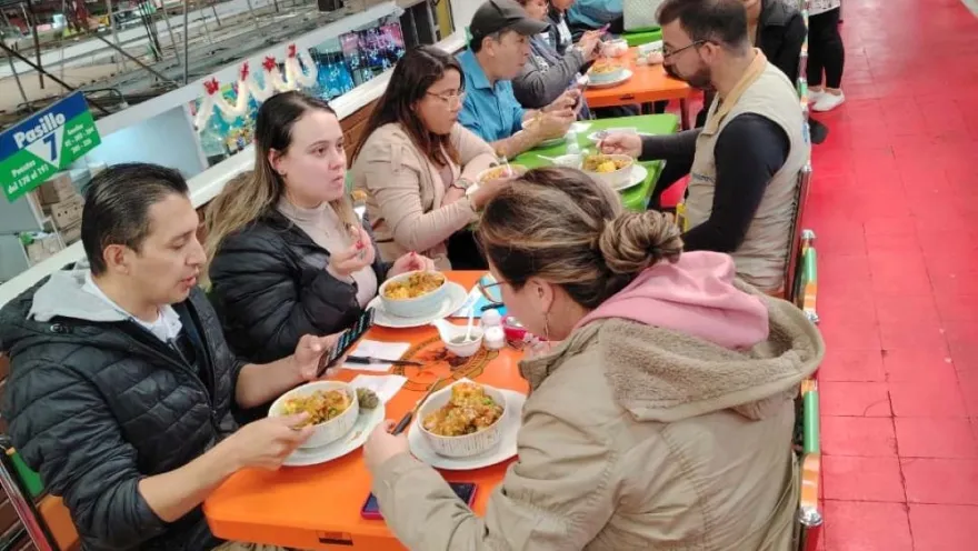Grupo de personas en un restaurante de una plaza de mercado comiendo productos tradicionales colombianos como sancocho y frijolada.