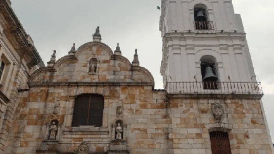  Iglesia de San Francisco fachada en primer plano en contrapicado, estructura entre piedra y concreto con puerta en madera ovalada. Destaca la superficie blanca de la torre del reloj y campanario.
