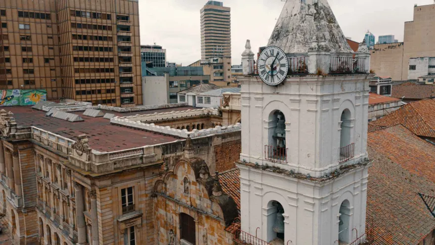 Iglesia San Francisco su blanca torre del reloj y campanario en primer plano y otros techos de edificaciones contiguas.
