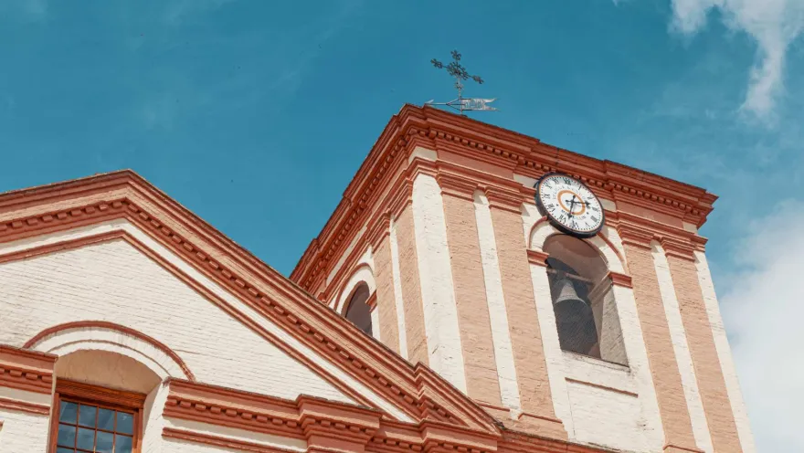Iglesia San Ignacio en primer plano en contrapicado de la torre del reloj y cruz de metal. El cielo es azul.