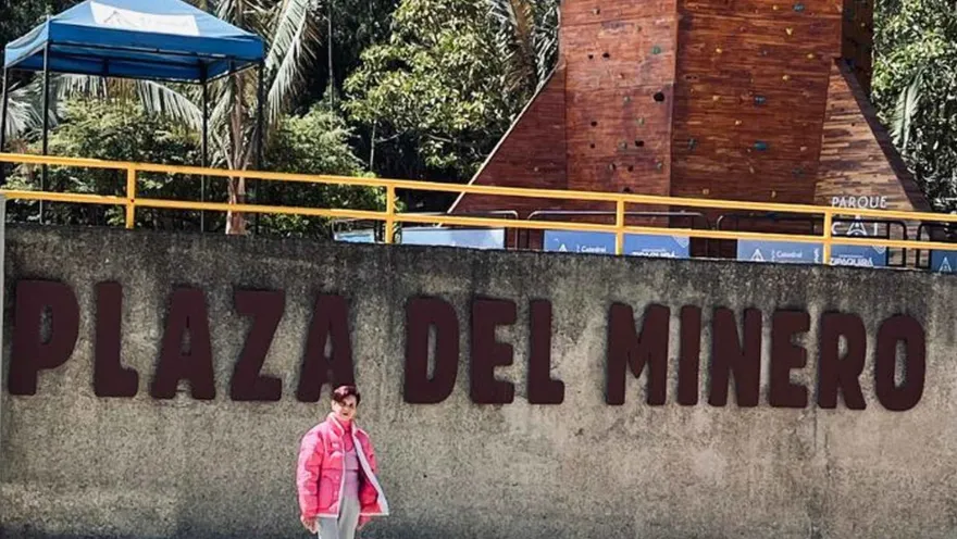 Mujer adulta piel castaño y chaqueta rosa delante del letrero Plaza del Minero. 