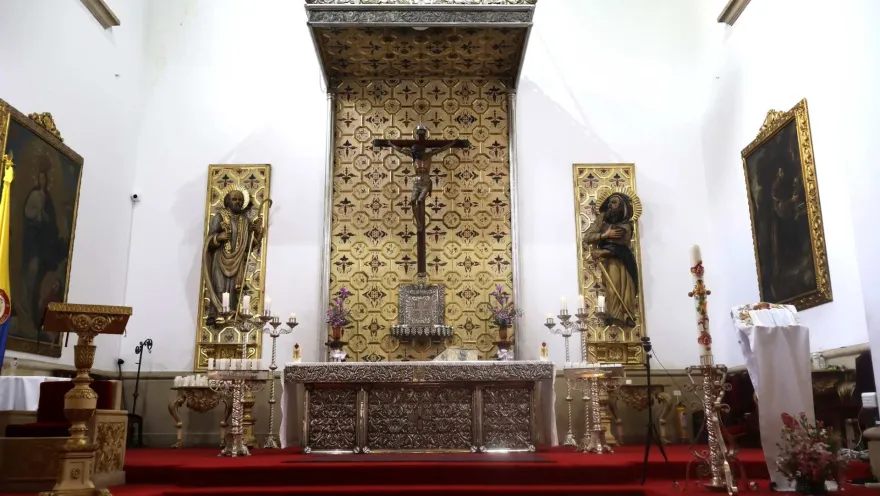 Iglesia de La Veracruz en su interior blanco con el altar con un Cristo en el centro y dos figuras religiosas a los lados. El psio está cubierto con un tapeqte roj.