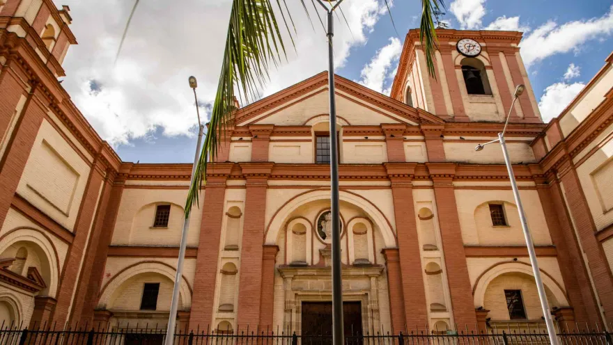Iglesia San Ignacio en primer plano de frente a la fachada. Al frente hay tres postes eléctricos, dos ramas de palma y el cielo azul.