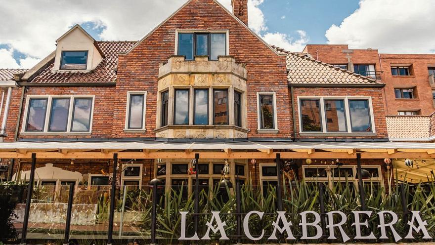 Esta fotografía se centra en la fachada de un emblemático restaurante de la Zona G. La construcción, hecha de ladrillo rojo, tiene un estilo de casa inglesa que le da un aire clásico y acogedor. En la parte inferior, se distingue el nombre del restaurante, La Cabrera. Las luces que cuelgan del toldo sugieren que el lugar cobra vida también de noche, prometiendo una experiencia gastronómica de alto nivel.