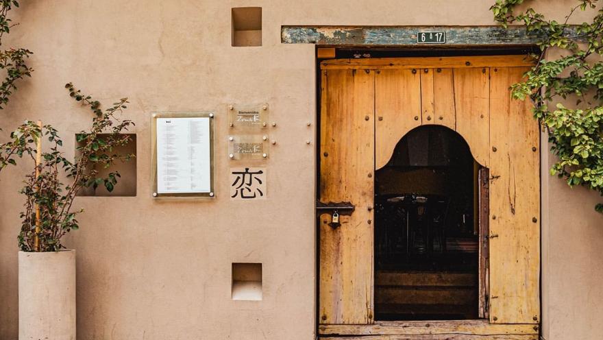 Fachada de un restaurante de estilo rústico en Usaquén, con una puerta de madera tallada que evoca la tradición y la cultura de la zona. Al lado, un menú da la bienvenida a los visitantes.