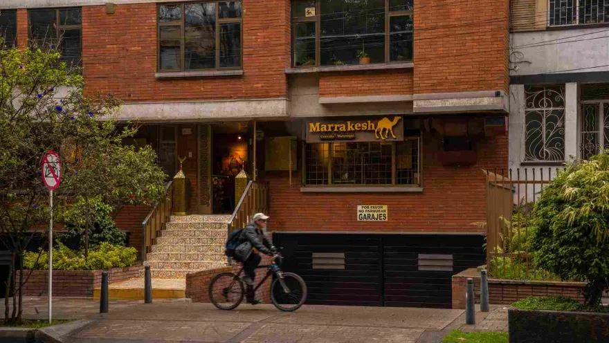 The photograph shows the entrance to 'Marrakech', a restaurant with a red brick facade on Park Way. The main door is flanked by a tiled staircase with gilded railings, giving it an exotic touch. The restaurant sign, with the name in Arabic script and the silhouette of a camel, evokes Moroccan culture.