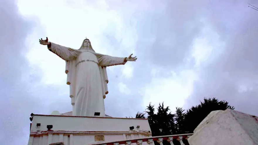 Sendero Guadalupe - Aguanoso con imágen de la Virgen de Guadalupe y sus brazos abiertos en contrapicado con cielo gris.