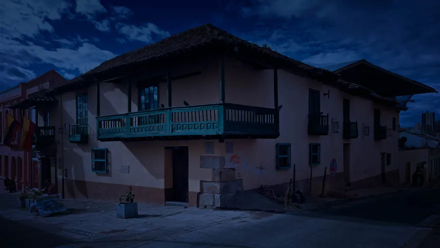Casa esquinera colonial fachada rosa con balcones verdes, dos palomes sobre el principal y un tono azul como de anochecer. 