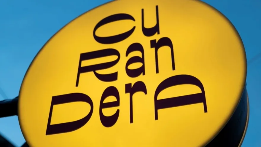  Aviso gigante de forma circular de color amarillo con letras en café que dice "curandera". 