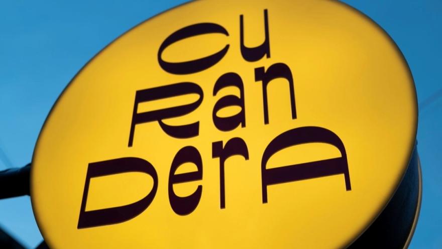  Aviso gigante de forma circular de color amarillo con letras en café que dice "curandera". 