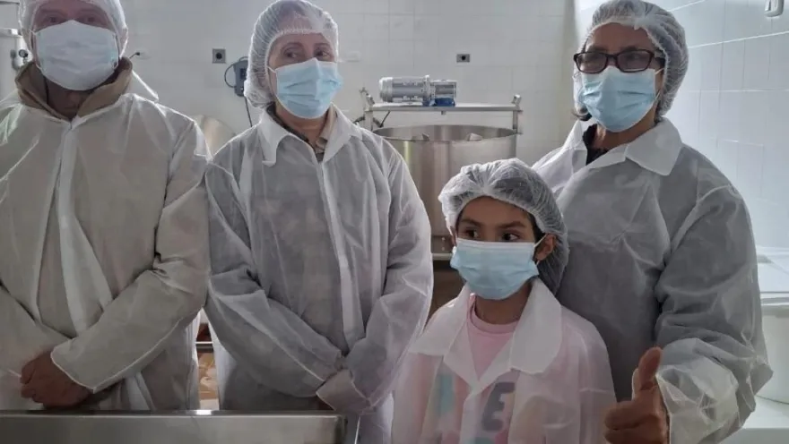 un hombre, dos mujeres y un niño con cofias y tapabocas en una cocina industrial.