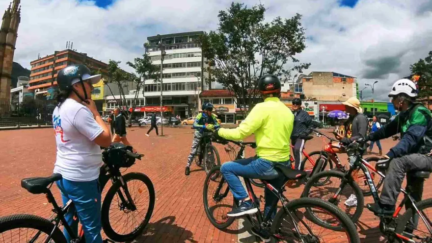 Grupo de ciclistas en la plazoleta de Lourdes, encima de sus bicicletas escucha a un guía.