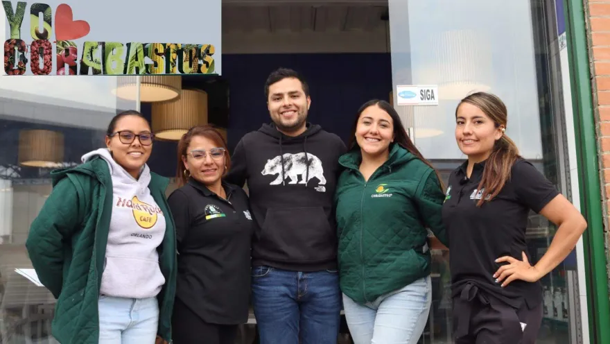 Grupo de cuatro mujeres y un hombre que abrazados sonríen. Hay un logo que dice yo amo Corabastos