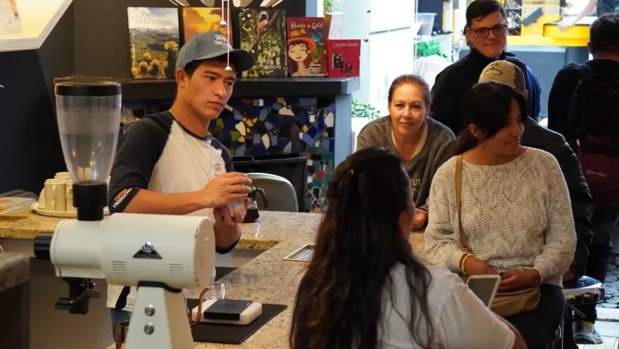 Grupo de personas jóvenes observan a un joven que prepara café. hay una máquina de preparar café sobre una mesa.