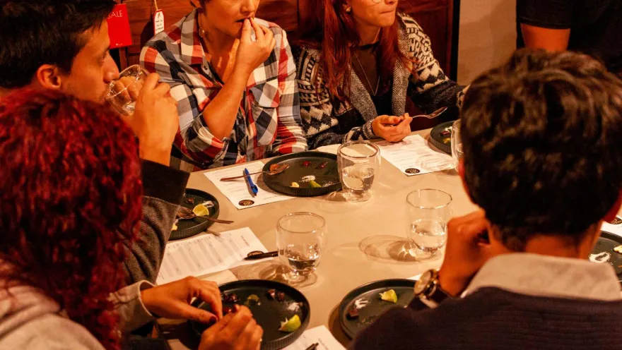 Grupo de personas jóvenes alrededor de una mesa, catando trozos de café y tomando anotaciones en una hoja de papel.