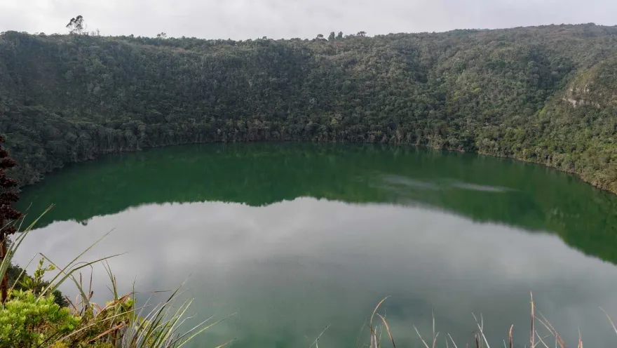 Laguna de Guatavita circular con agua verde y rodeada por frondosa vegetación.