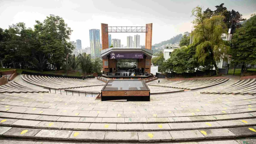 Open-air brick theater, daytime view. Steps leading to the stage are visible, covered by a roof, two brick columns, and a large sign reading ""Idartes.""