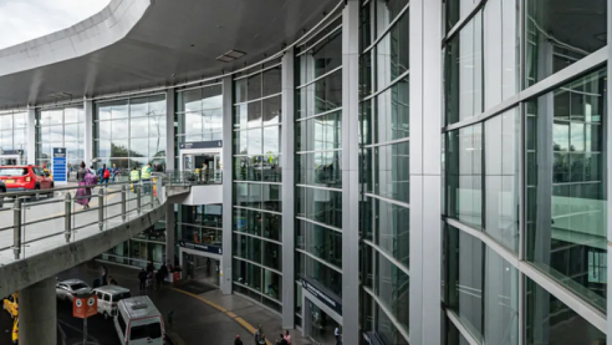 Exterior of a two-story building. Several vans are parked on the ground floor. On the second floor, there is a pedestrian bridge with some people walking across it.