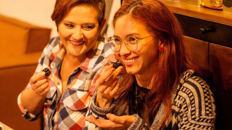 Dos mujeres en primer plano sonríen mientras están comiendo algo.