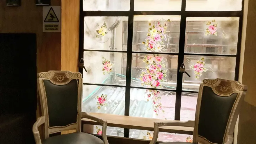 An indoor living room with two antique chairs in good condition and a large window at the back featuring colorful rose designs.