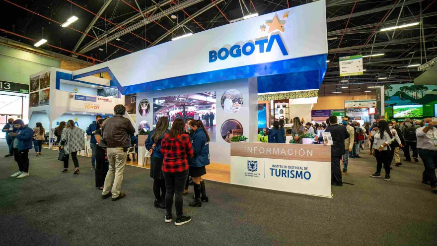 An event hall with a large booth that reads "Bogotá, District Tourism Institute." People are gathered around.