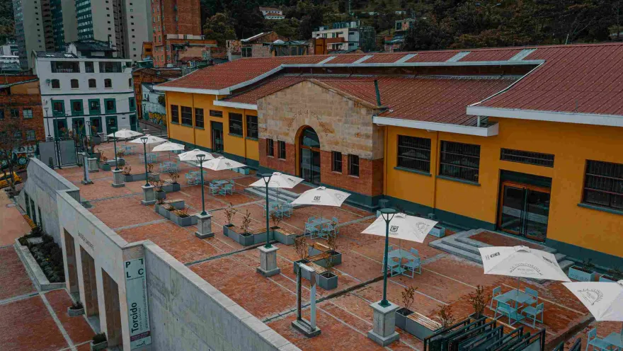 Plaza de Mercado La Concordia vista desde arriba, con varias mesas con parasoles. Al fondo se observan árboles y edificios.