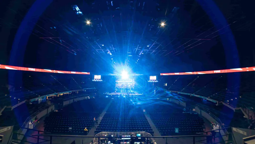 Inside the arena, showing empty stands and a beam of bright blue light emanating from the stage.