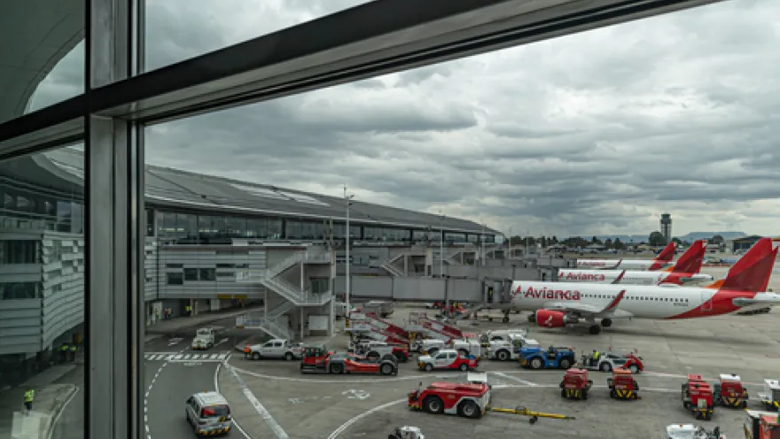 Interior window of an airport showing some Avianca airplanes parked on the ground.