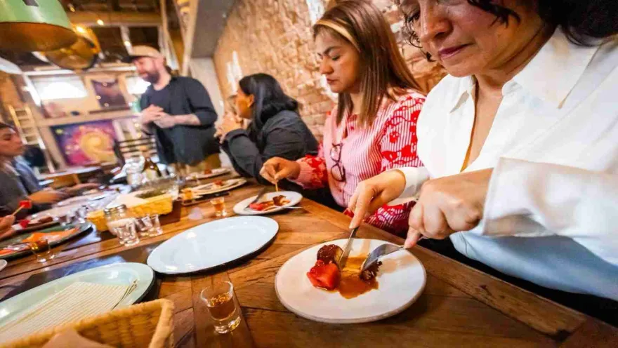 Tres mujeres jóvenes sentadas alrededor de una mesa degustando un postre. En la mesa hay copas de cristal con licor.