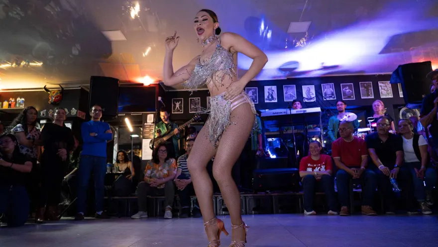  Una mujer con un taje de bailarina blanco baila frente a varias personas.