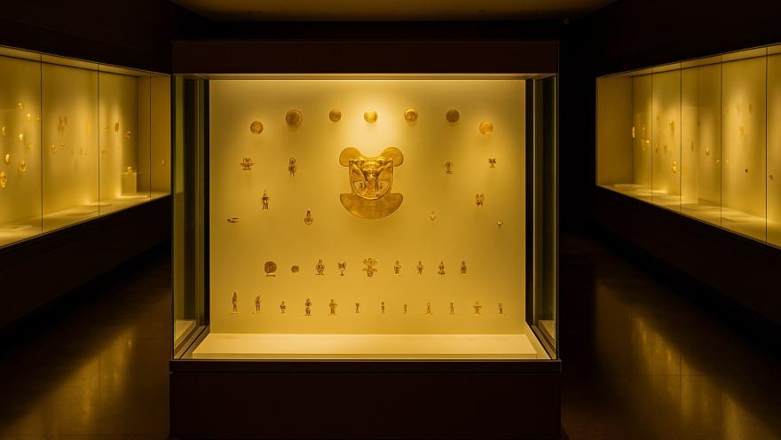 Interior del Museo del Oro en un salón oscuro en donde se iluminan piezas doradas en una vitrina.