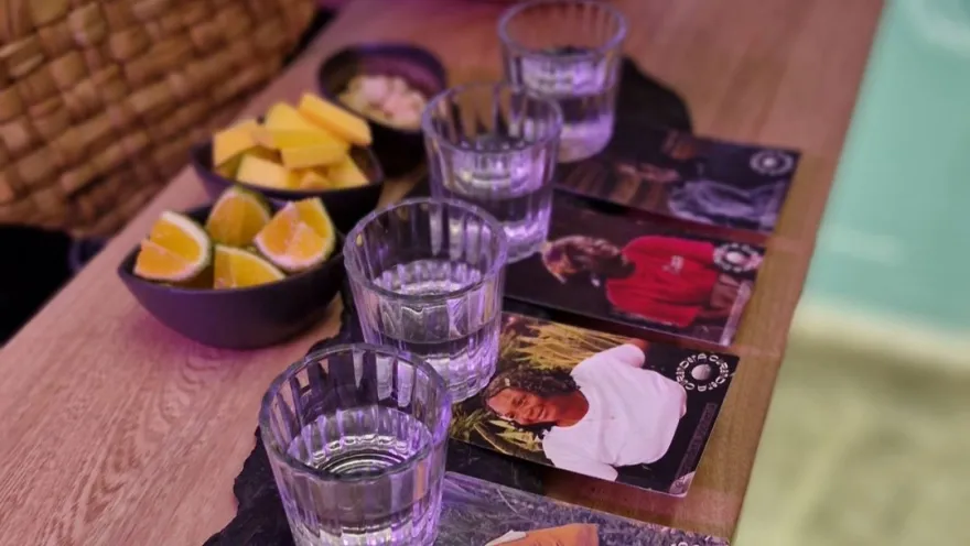 primer plano de cuatro copas pequeñas de cristal con un líquiso blanco que parece ser licor. Las copas están sobre unos portavasos con rostros de personas afrodescendientes.