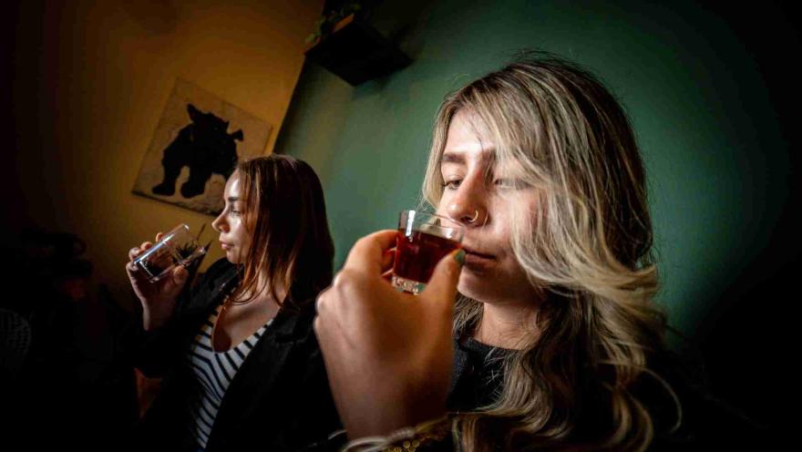  Dos Mujeres jóvenes huelen cada una, el contenido líquido de una copa de cristal.