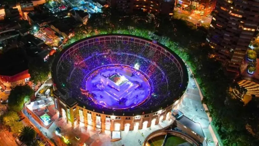Vista interior desde arriba y de noche de la Plaza La Santamaría, una estructura circular rodeada por árboles y que está iluminada en su centro.