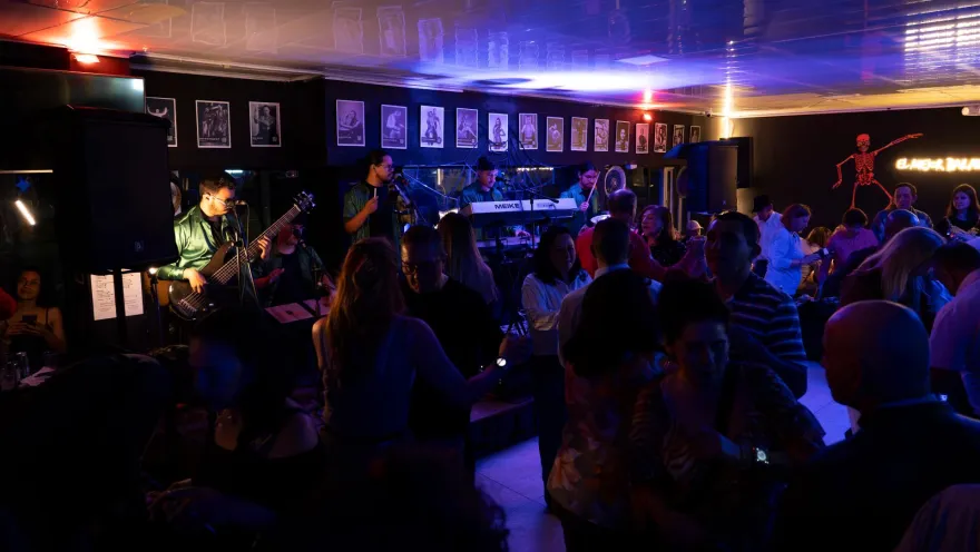 Grupo de adultos en un salón están bailando al lado de una banda musical.