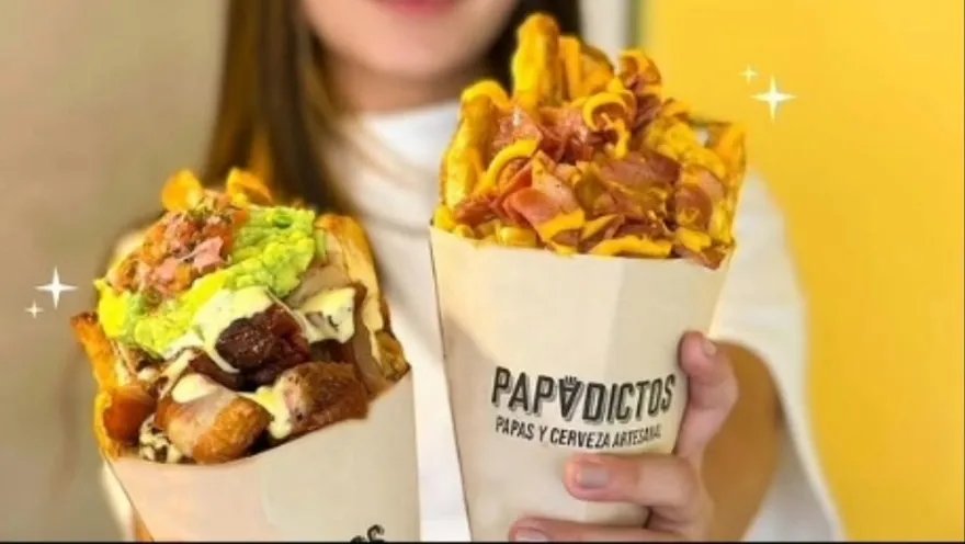Primer plano de dos paquetes de papas a la francesa con salsas y otros trozos de comida rápida.