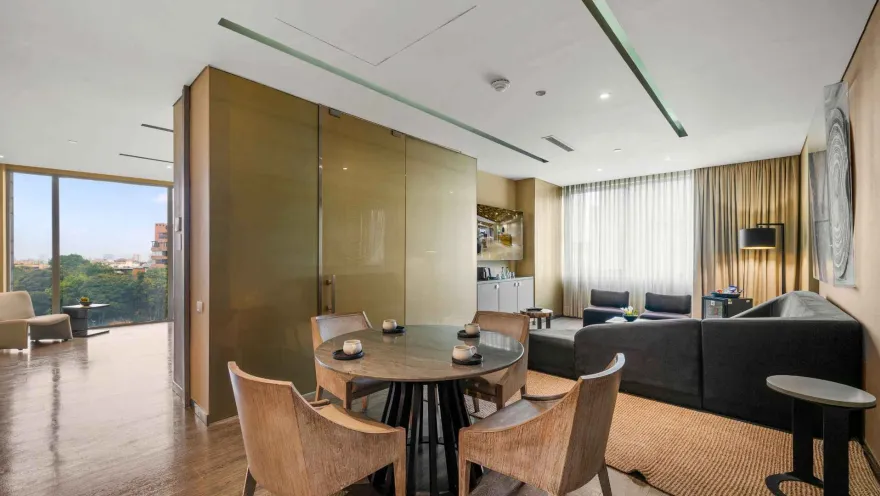 Un área de sala de estar moderna y espaciosa con un sofá en forma de L, una mesa redonda con sillas y grandes ventanales que ofrecen vistas.