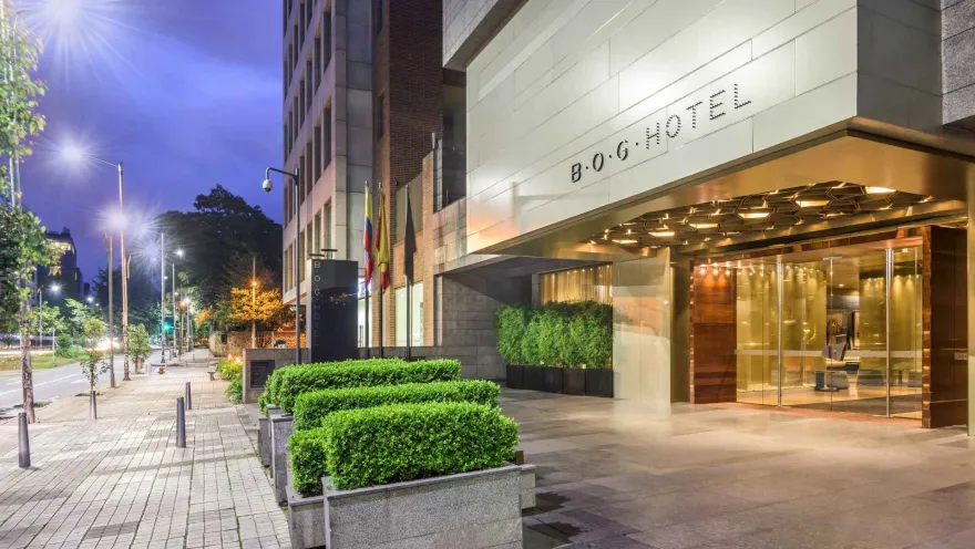 La entrada del B.O.G. Hotel al anochecer, con una arquitectura moderna, setos bien cuidados y una iluminación elegante que realza su fachada.