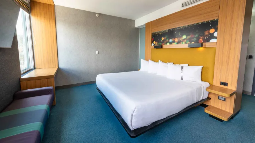 Una habitación de hotel Aloft moderna y colorida con una cama king-size, una ventana con banco y un cabecero decorativo con luces.