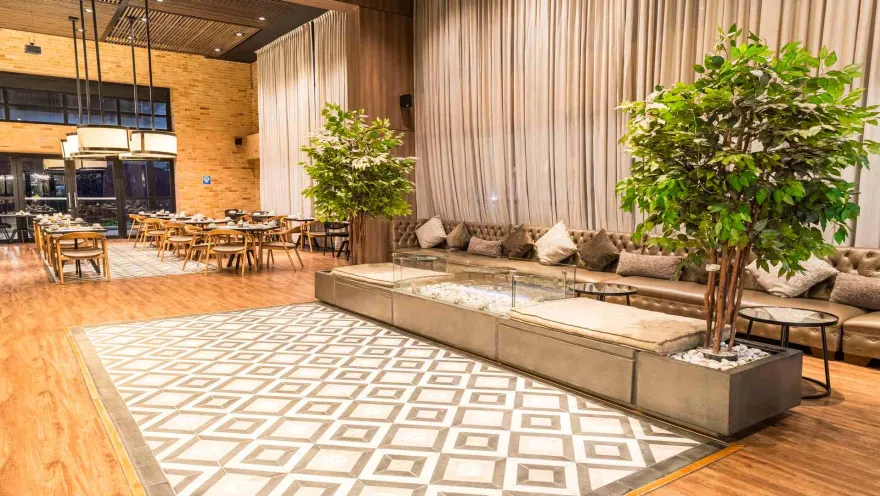 Lobby moderno de hotel con sofás, árboles decorativos y un restaurante al fondo.