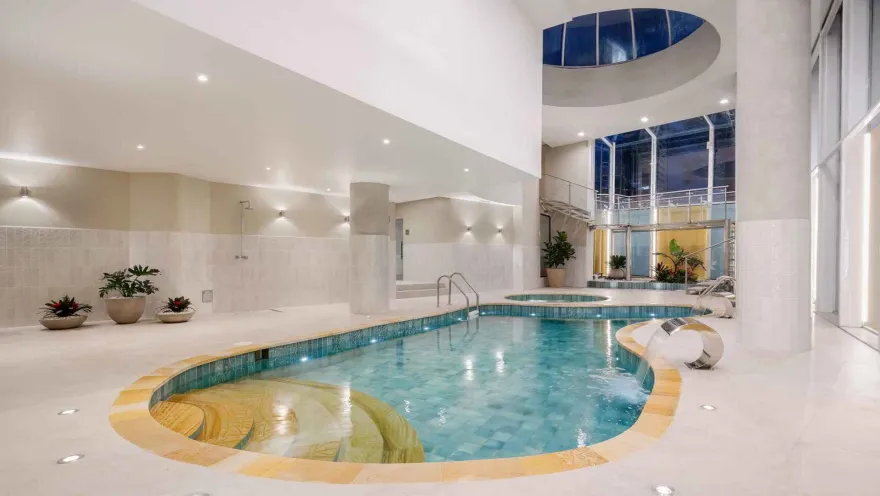 Piscina cubierta de forma orgánica con jacuzzi y escalera de caracol, techo alto.