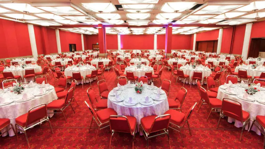 Gran salón de eventos con mesas redondas y sillas rojas. Ideal para banquetes o conferencias.