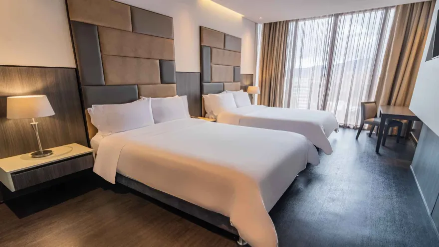Una habitación de hotel con dos camas dobles, cabeceras acolchadas y una decoración moderna. Las cortinas de suelo a techo enmarcan la vista exterior.